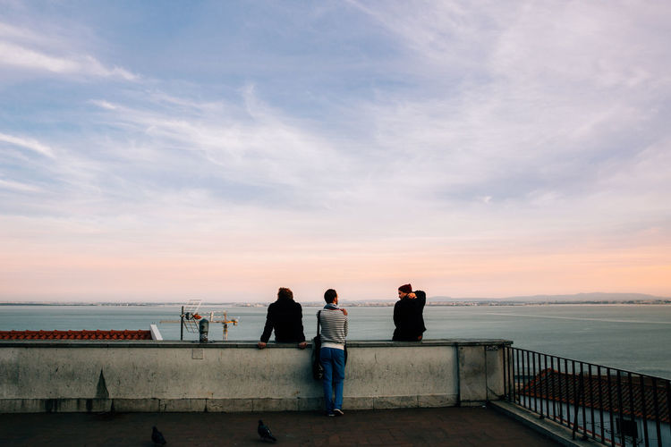 People standing by sea against sky during sunset