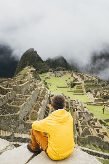 A man in a yellow jacket is sitting near ruins of machu picchu, peru