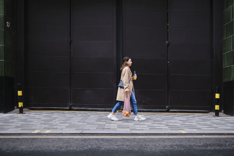 Young woman walking on footpath by black doors