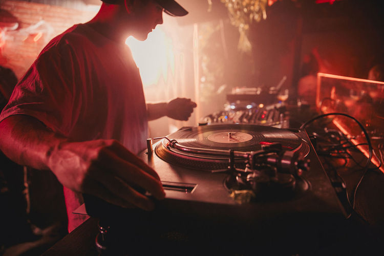Side view of crop male dj mixing music on controller during concert in dark nightclub