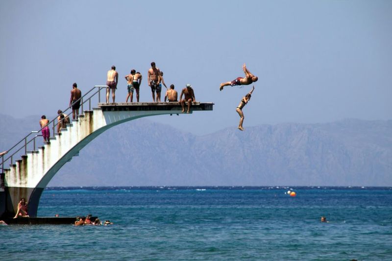 People jumping from diving platform in sea against clear sky