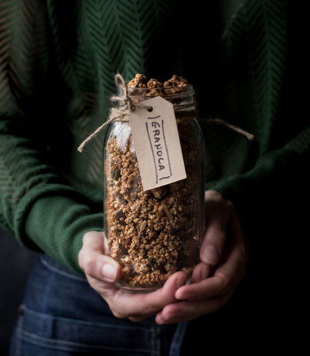 Unrecognizable female carrying glass jar of fresh millet and quinoa granola with label