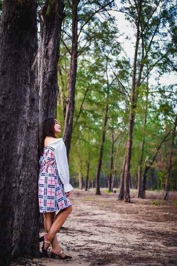 Woman standing by tree trunk in forest