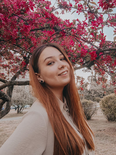 Portrait of smiling young woman standing against trees