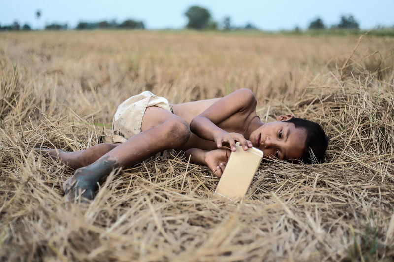 Boy using mobile phone while lying on field at farm