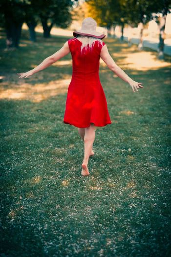 Rear view of woman wearing red dress walking on grass