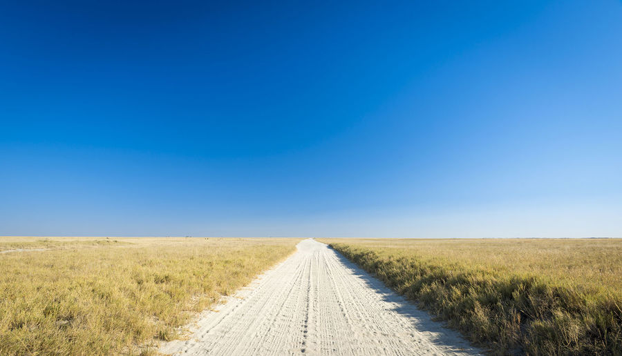 Road amidst field against clear blue sky
