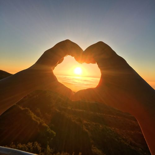 Close-up of cropped hands making heart shape against sun at sunset