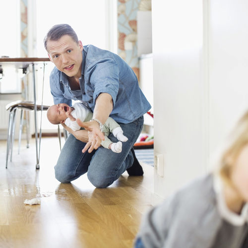 Father holding crying baby while stopping daughter on floor at home