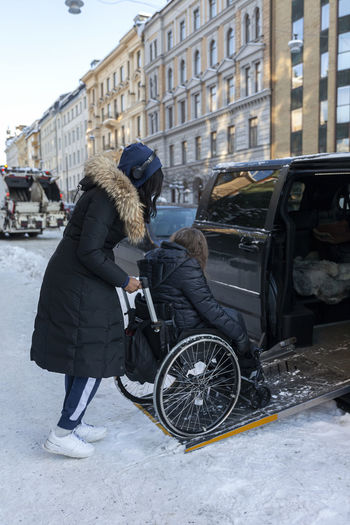 Carer helping woman on wheelchair to get into car