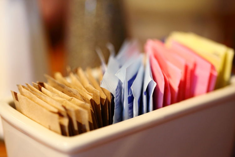 Close-up of sugar and sweetener packets in container at cafe