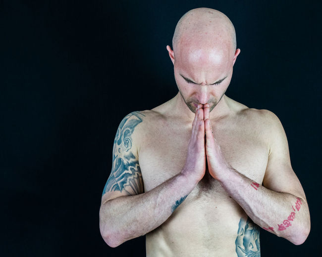 Shirtless bald man praying against black background