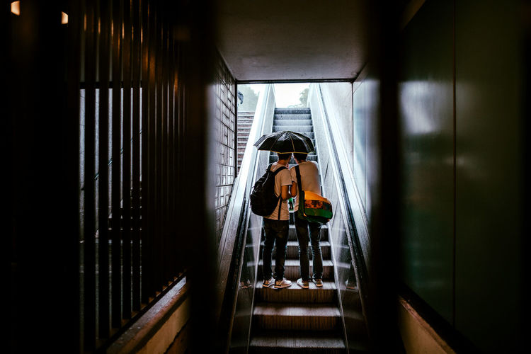 Rear view of two people standing on escalator