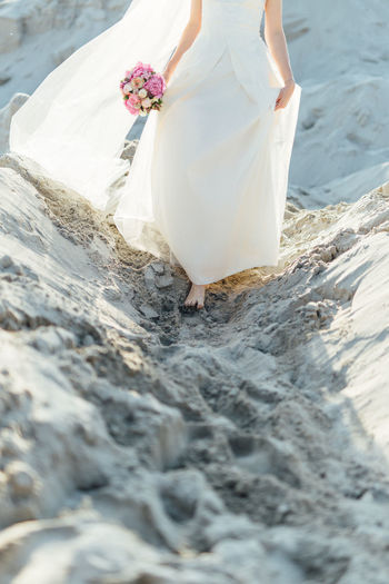 Low section of woman walking with bouquet on sand