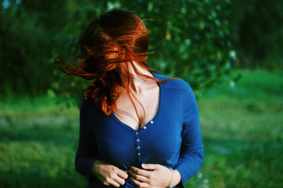 Redhead woman standing against tree at park