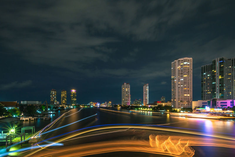 Light trail over chao phraya river against cloudy sky