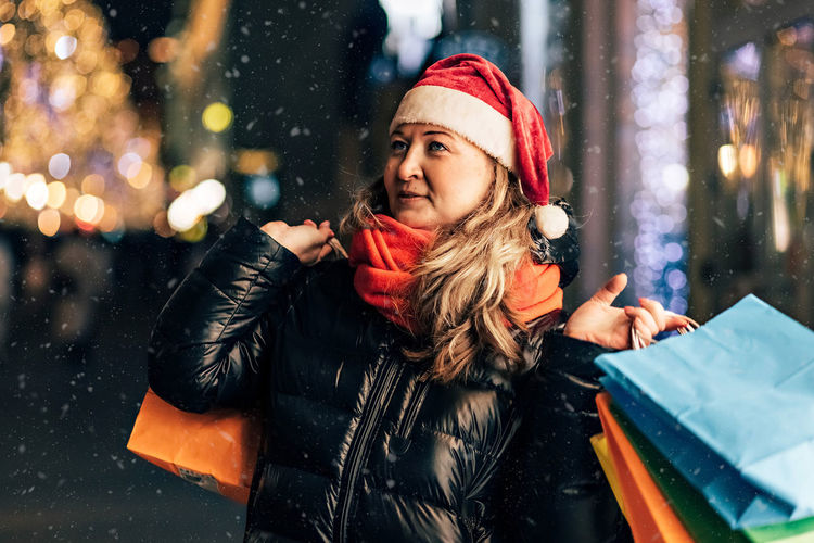 A woman in a santa hat with christmas shopping in colorful bags on the street decorated christmas 