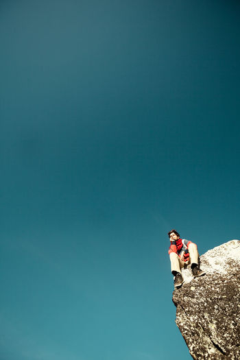 Low angle view of person on rock against clear blue sky
