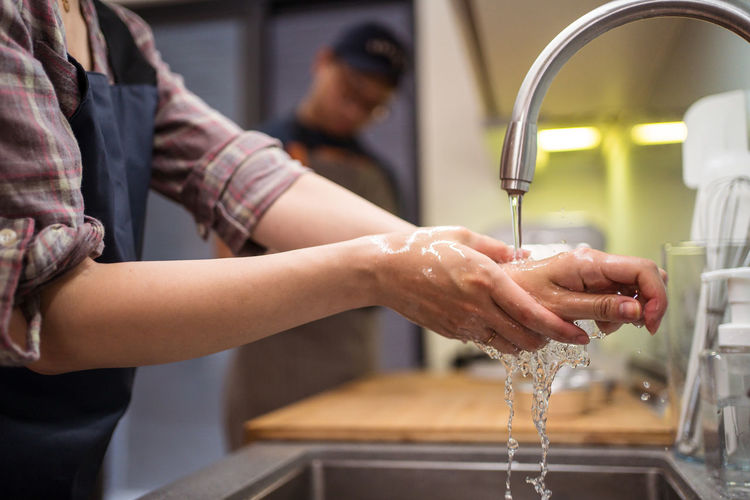 Cropped side view of woman washing hands in sink while having home bakery with man