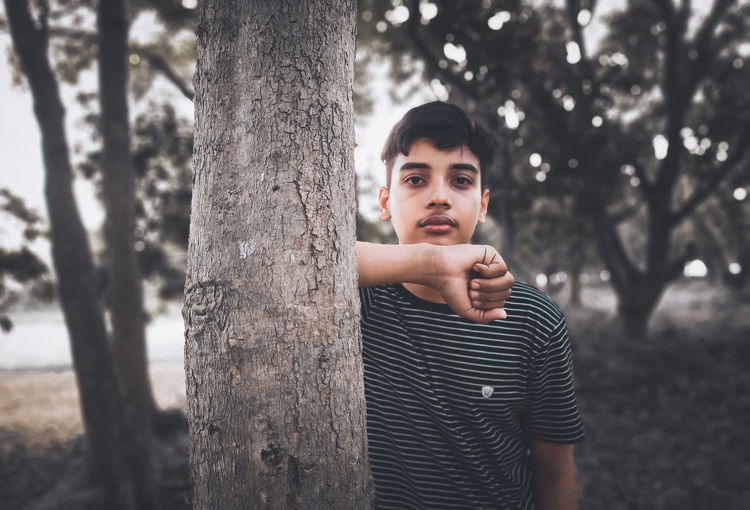Portrait of teenage boy standing on tree trunk