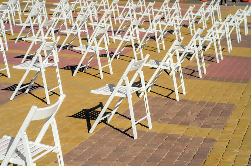 White folding chairs are placed on the square on pavement. quarantine restrictions