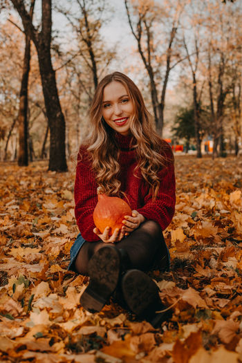 Portrait of beautiful woman sitting on tree during autumn