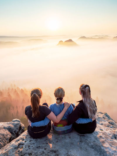 Three girls friends hug each other on sharp cliff. amazing misty morning and natural daybreak show