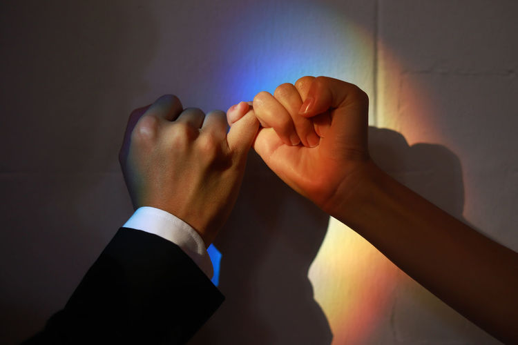 Cropped hands of couple hands taking pinky promise against wall