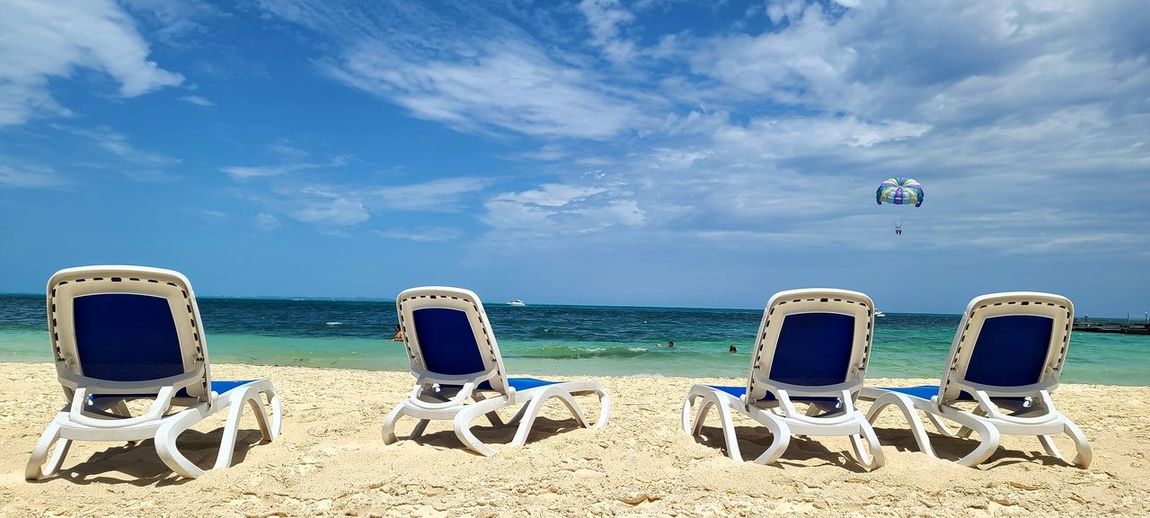 Deck chairs on beach against sky
