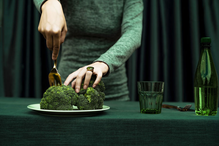 Midsection of woman cutting broccoli with fork kept in plate on table