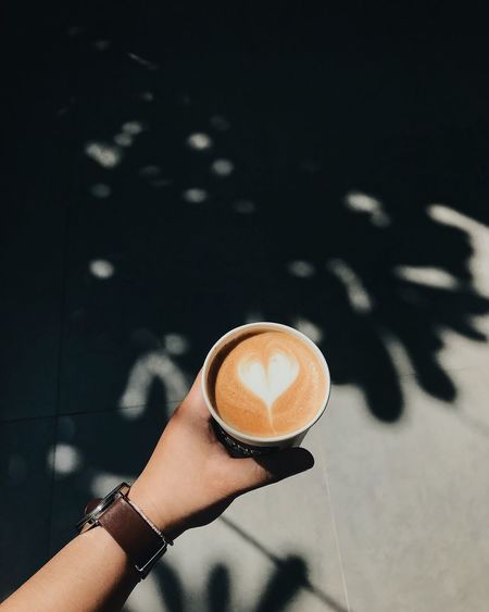 Cropped hand holding cappuccino over footpath