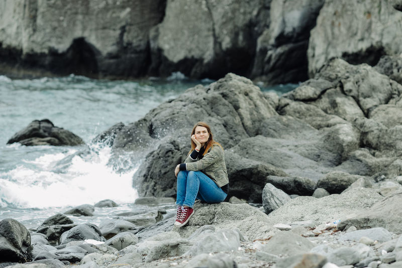 Young woman on rocks near stormy oceans. local tourism, solo travel. communication with nature.