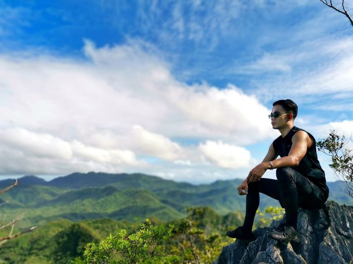 Man sitting on rock looking at mountains against sky