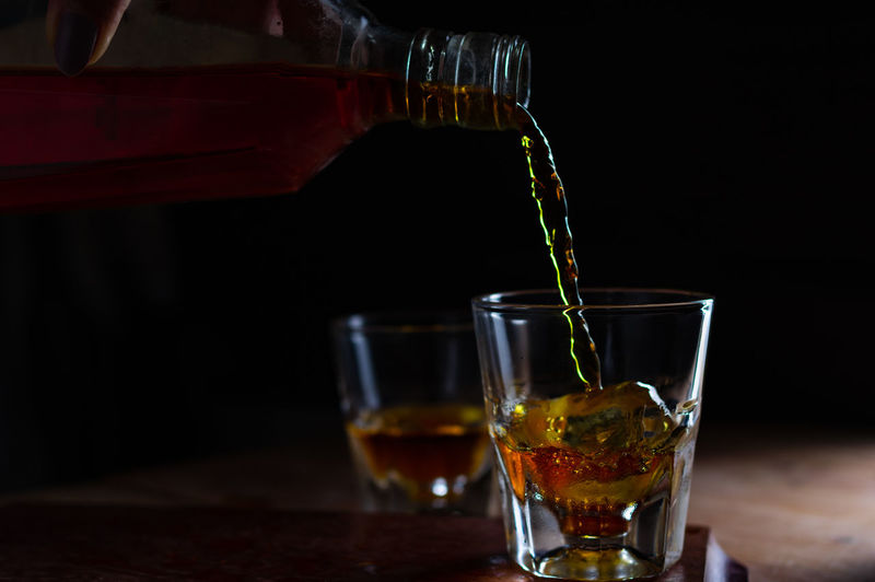 Close-up of pouring whiskey to the glass of ice 