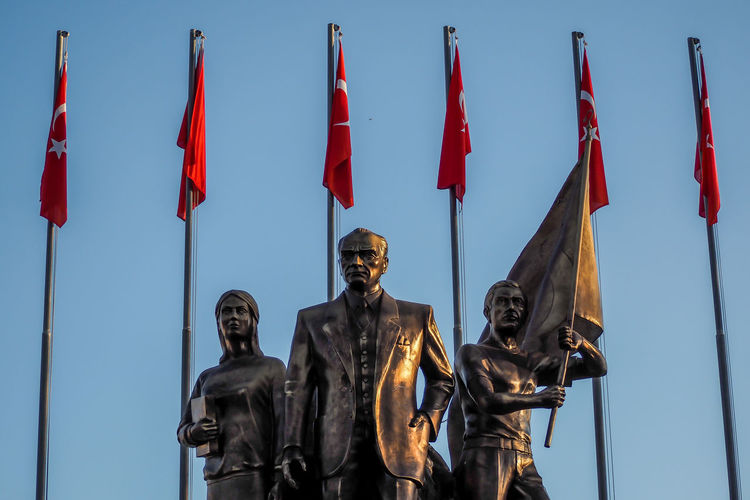 Low angle view of statues and red flags against sky