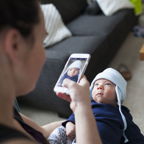 Mother photographing son through mobile phone at home
