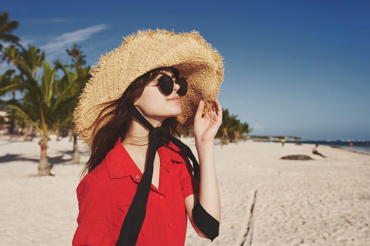 Young woman wearing sunglasses standing on beach against sky