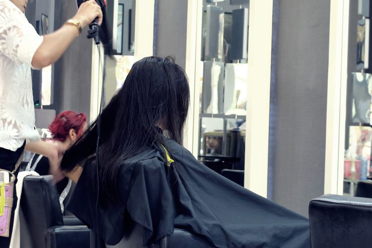 Midsection of hairdresser hairstyling customer at salon