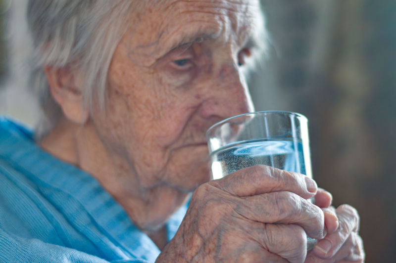 An elderly 90-year-old gray-haired woman who drinks water from a glass. loneliness, stress