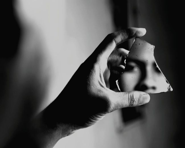Cropped image of man holding broken mirror with reflection