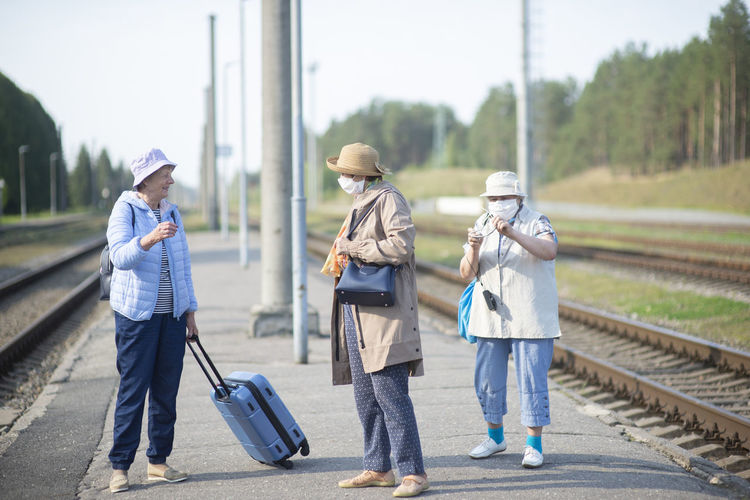 Three old senior women on  platform waiting for the train and wearing a face mask during a pandemic