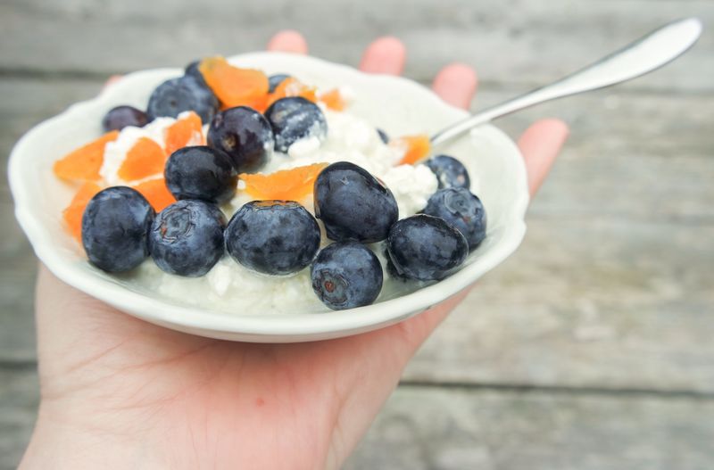 Cropped hand holding bowl of apricots and blueberries with cottage cheese