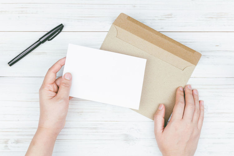 Cropped image of woman holding card with envelop on table