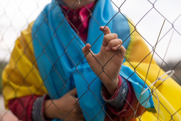 Sad little girl with the flag of ukraine behind a metal fence. social problem of refugees 