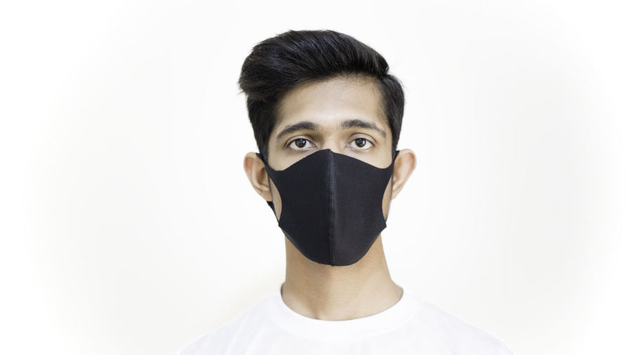 Portrait of young man covering face against white background