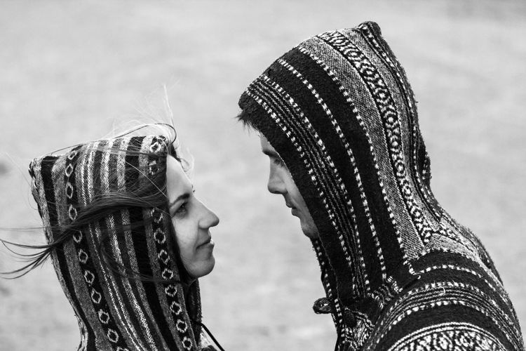 Side view of couple in hooded clothing looking at each other while standing on field