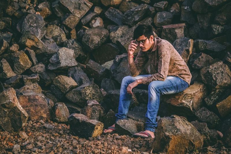 Thoughtful young man looking away while sitting on rock
