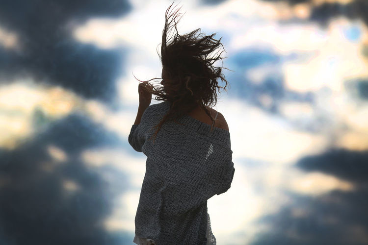 Rear view of woman tossing hair against sky