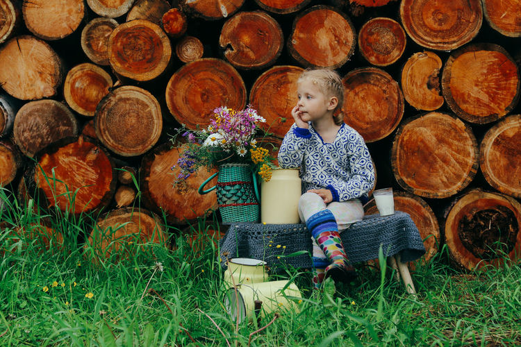 Rustic style, a girl in casual clothes sits on a bench against the background of a woodpile