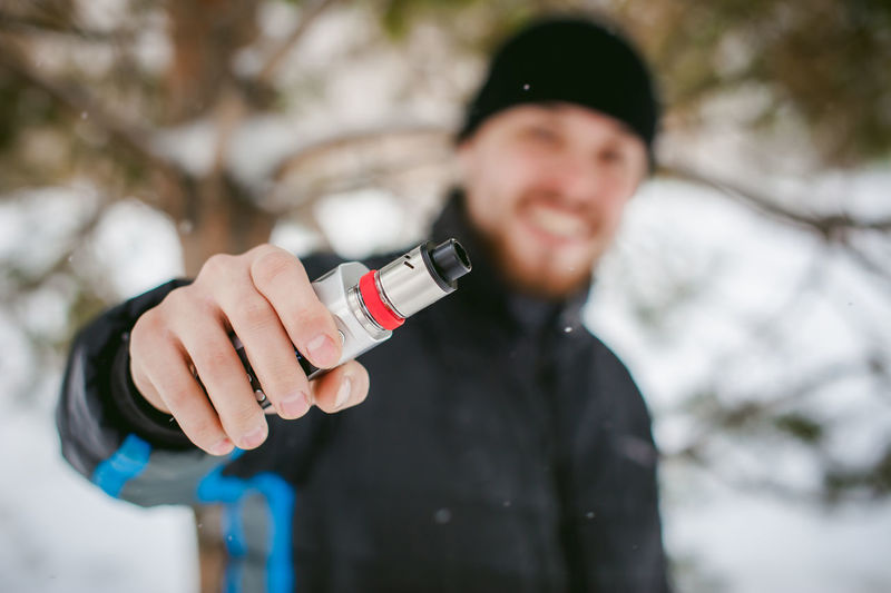 Close-up of man holding electronic cigarette on snow covered field